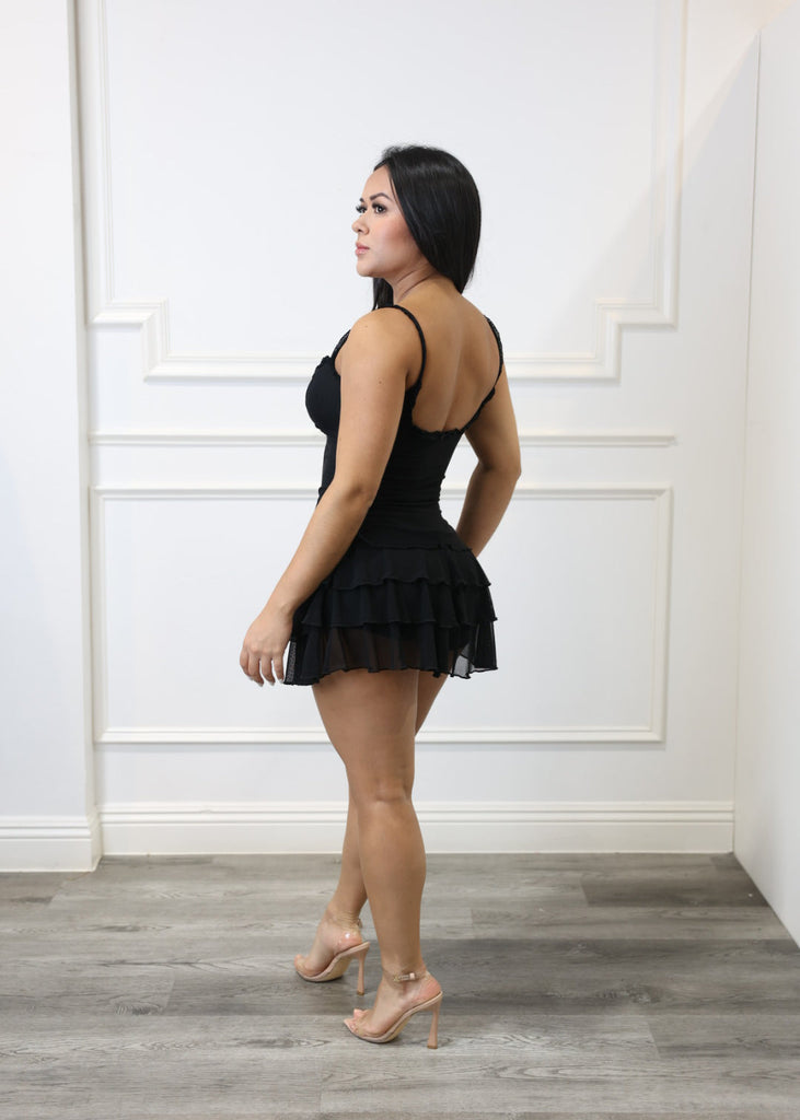 Woman in a black dress standing on a white floor with a wooden wall.
