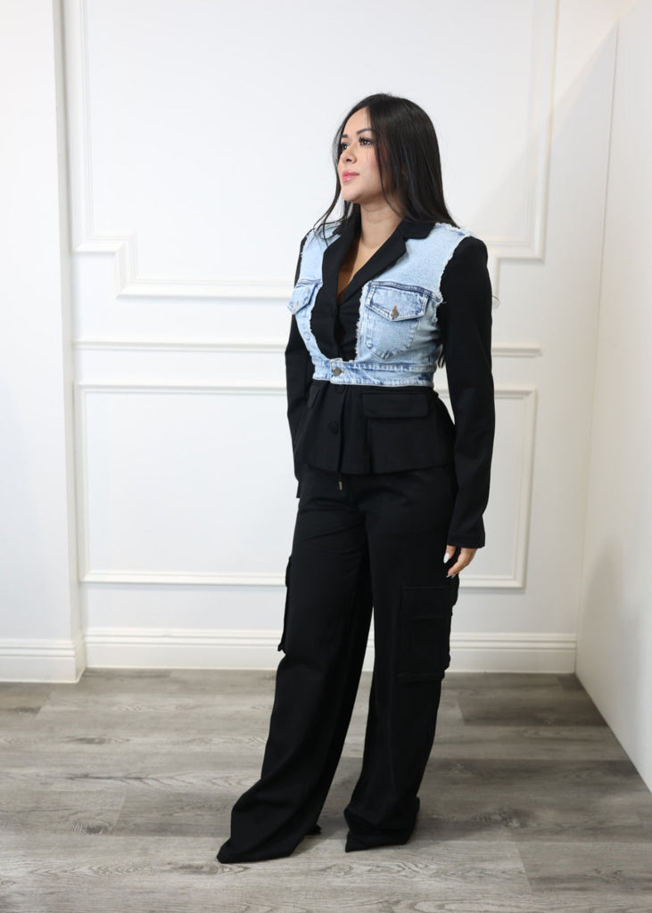 Person wearing a black outfit with a denim jacket in a minimal indoor setting