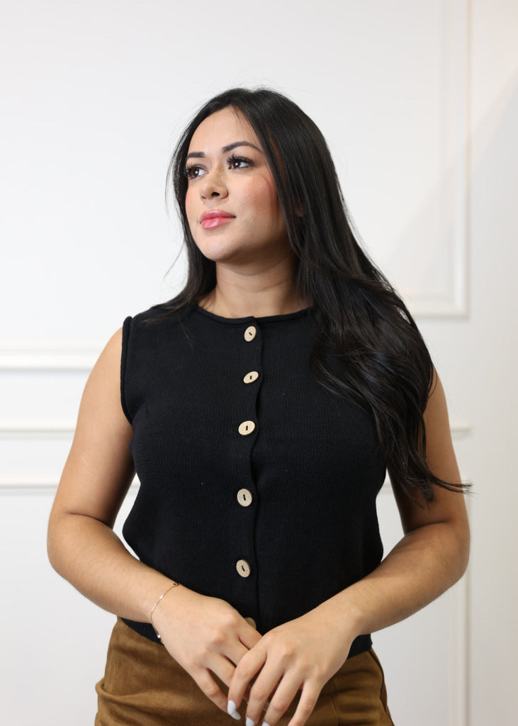 Woman wearing a black sleeveless top with gold buttons against a white background