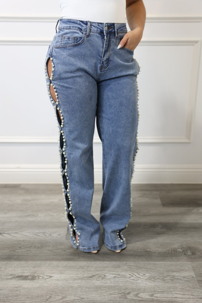 Person holding up a pair of blue jeans with decorative trim against a neutral background
